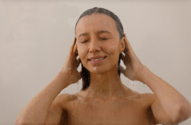 Young woman under the trickles of water in pleasure shower. Beautiful girl under the spray of water on isolated background. Wet happy face. Cold Showers Beat Vitamins