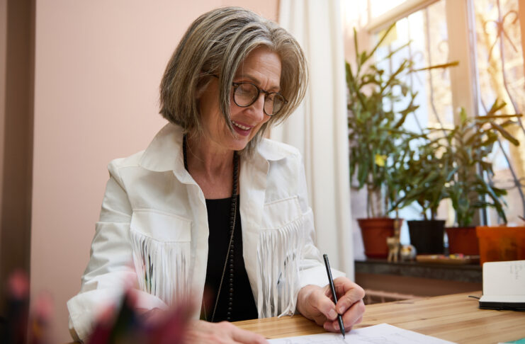 Fashion designer tailor dressmaker, elderly Caucasian business woman drawing sketches for clothes, creating a new line of dress collection in her cozy creative fashion design studio Your Handwriting Changed This Decade